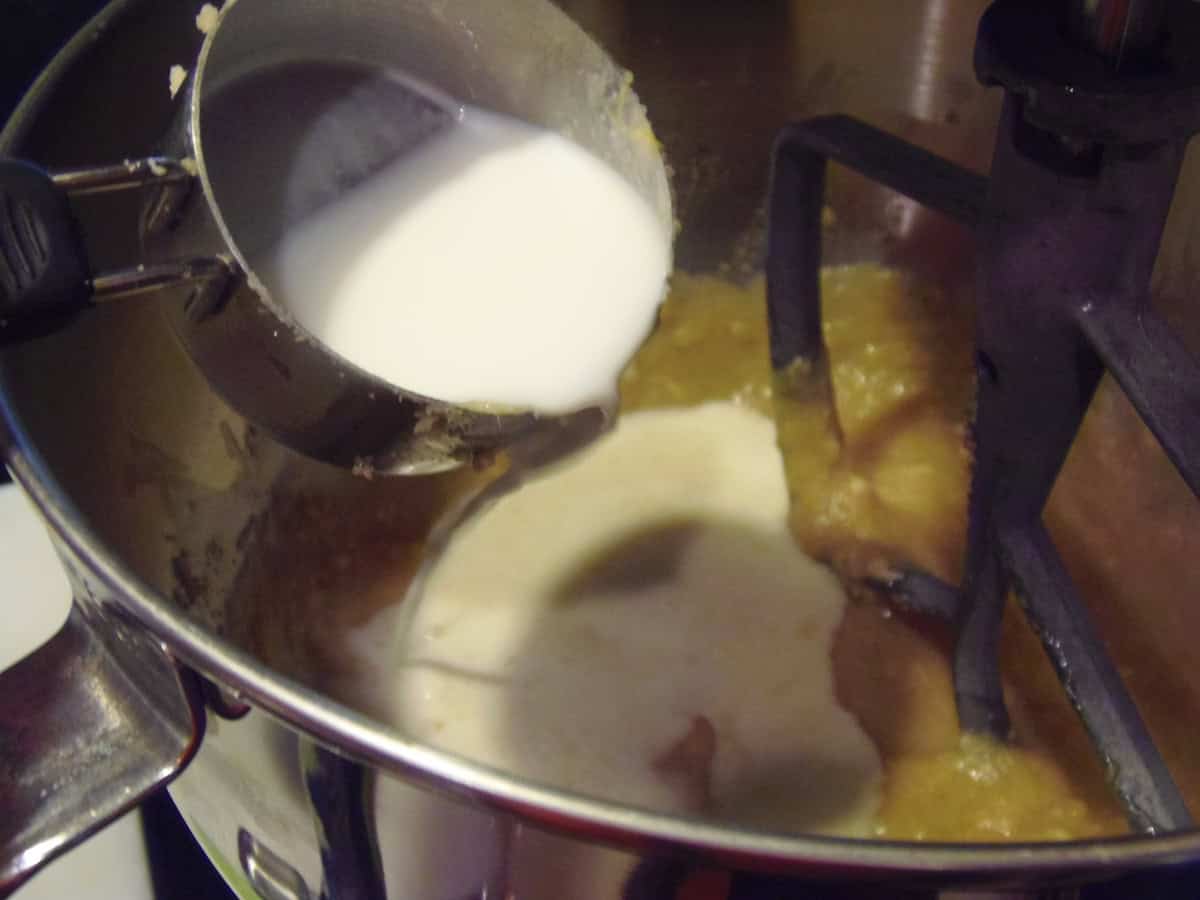Milk in a measuring cup being added to a stand mixer bowl with wet ingredients inside.