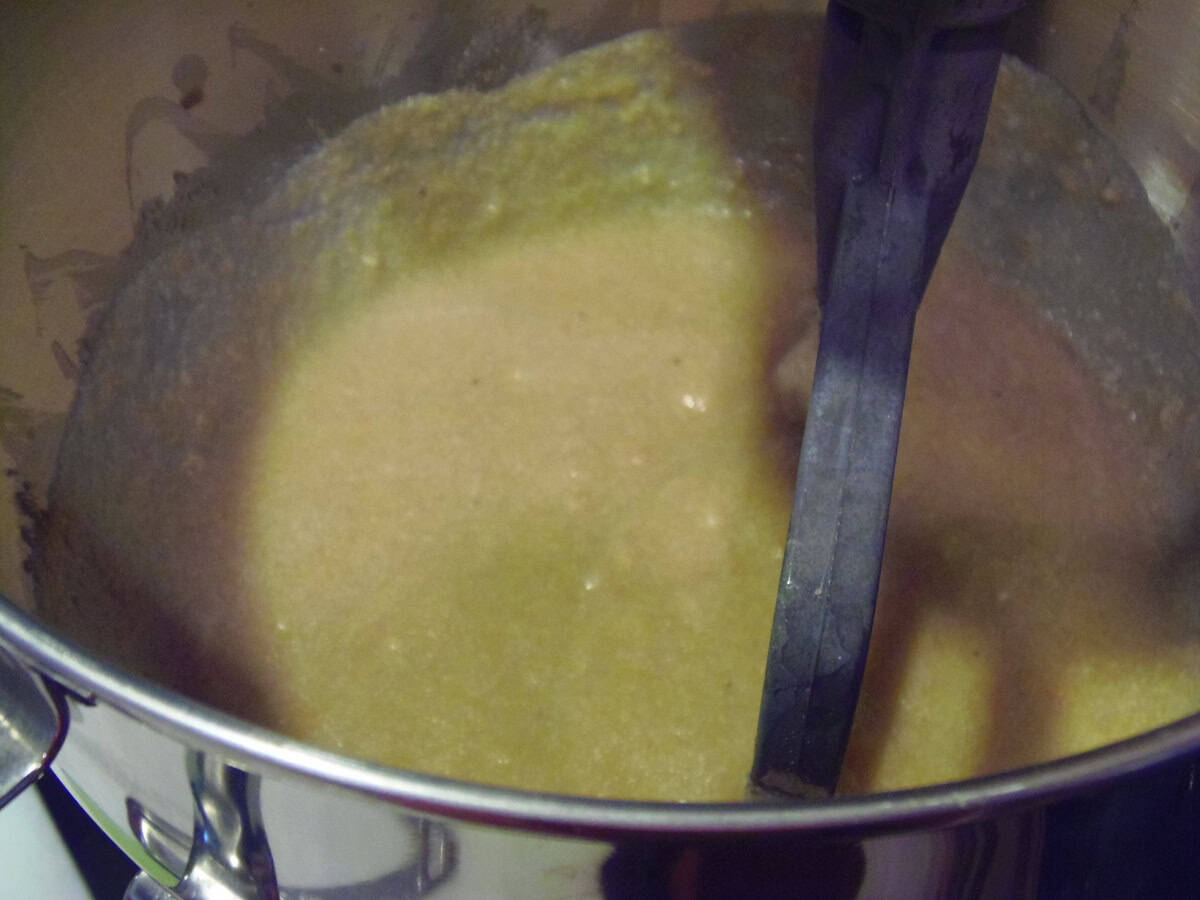 A paddle attachment inside a stand mixer bowl with wet ingredients for making donuts.