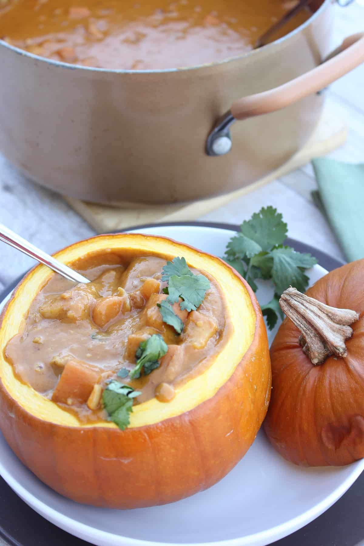 A spoon inside a pie pumpkin filled with pumpkin chicken stew.