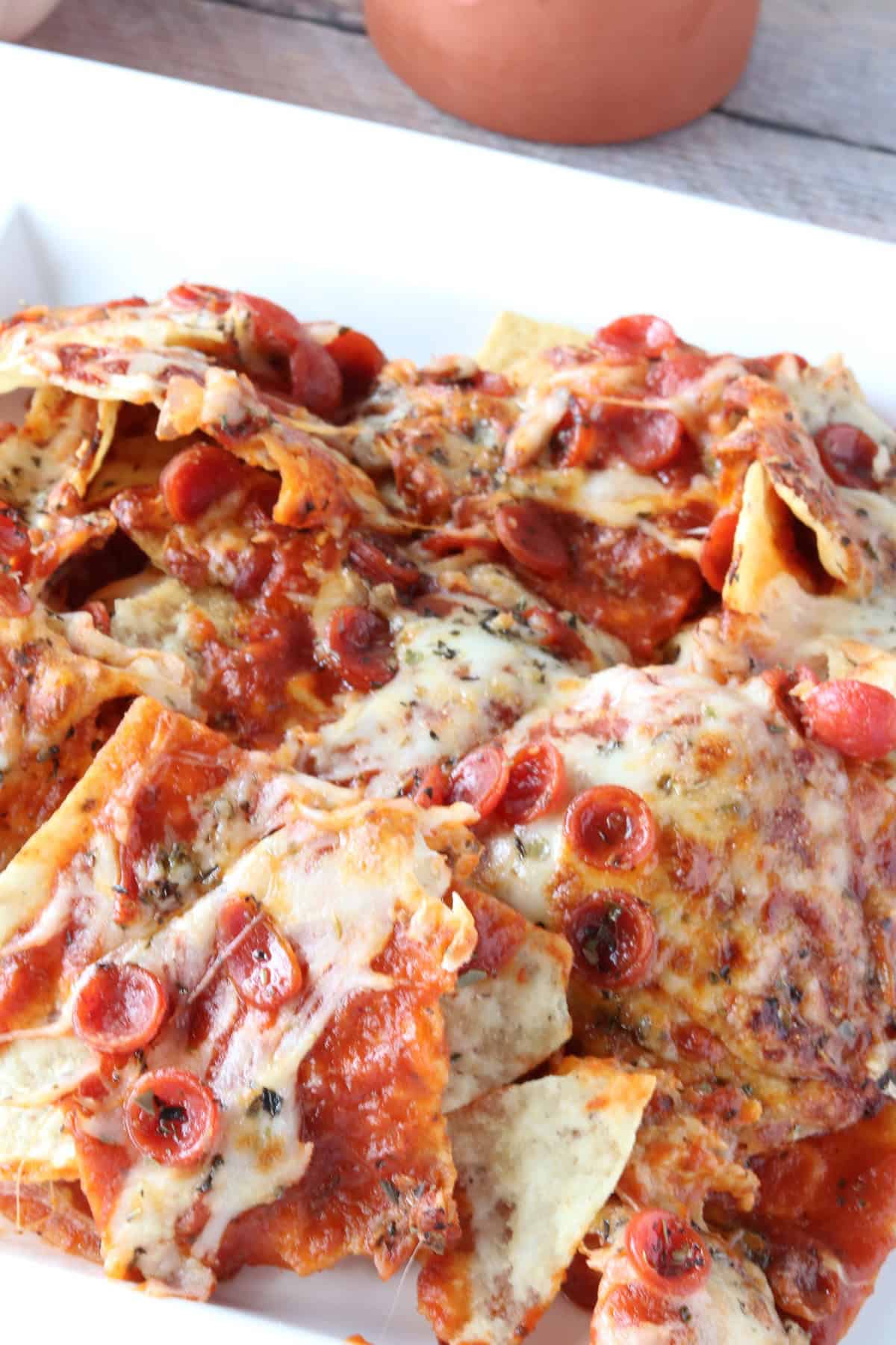 Pepperoni Pizza Nachos for the Air Fryer or Oven - kudoskitchenbyrenee.com Melted mozzarella cheese, Italian seasonings, and mini pepperoni pizza nachos on a plate.