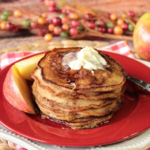 A stack of apple cider pancakes with butter sitting on a red plate.