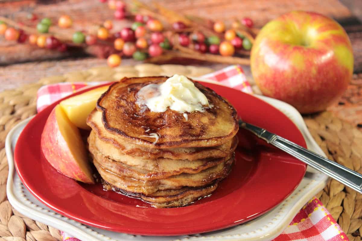 A fall scene for a plate of apple cider pancakes with butter and apple slices.