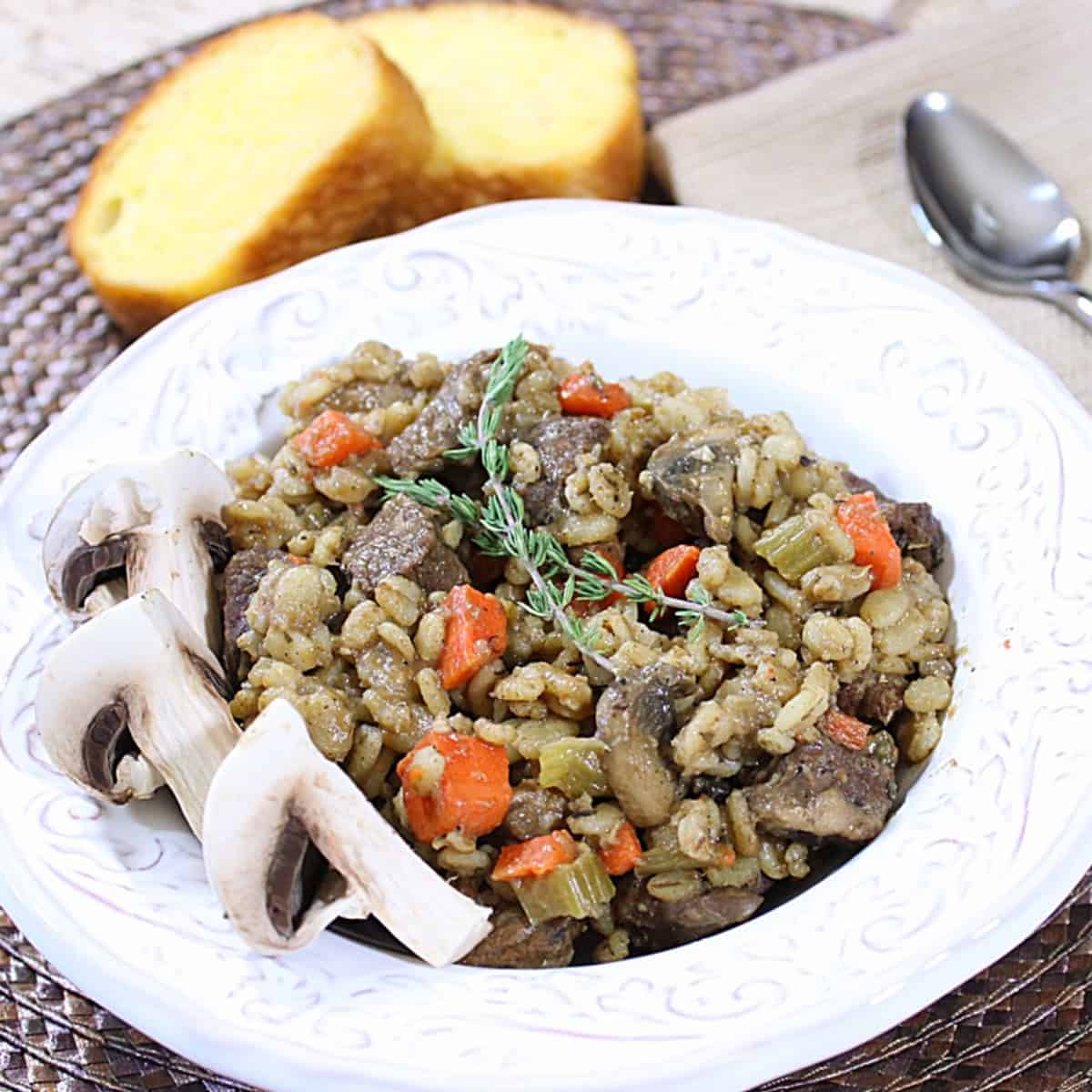 A delicious bowl of barley, beef and mushroom stew with a spoon and napkin on the side.
