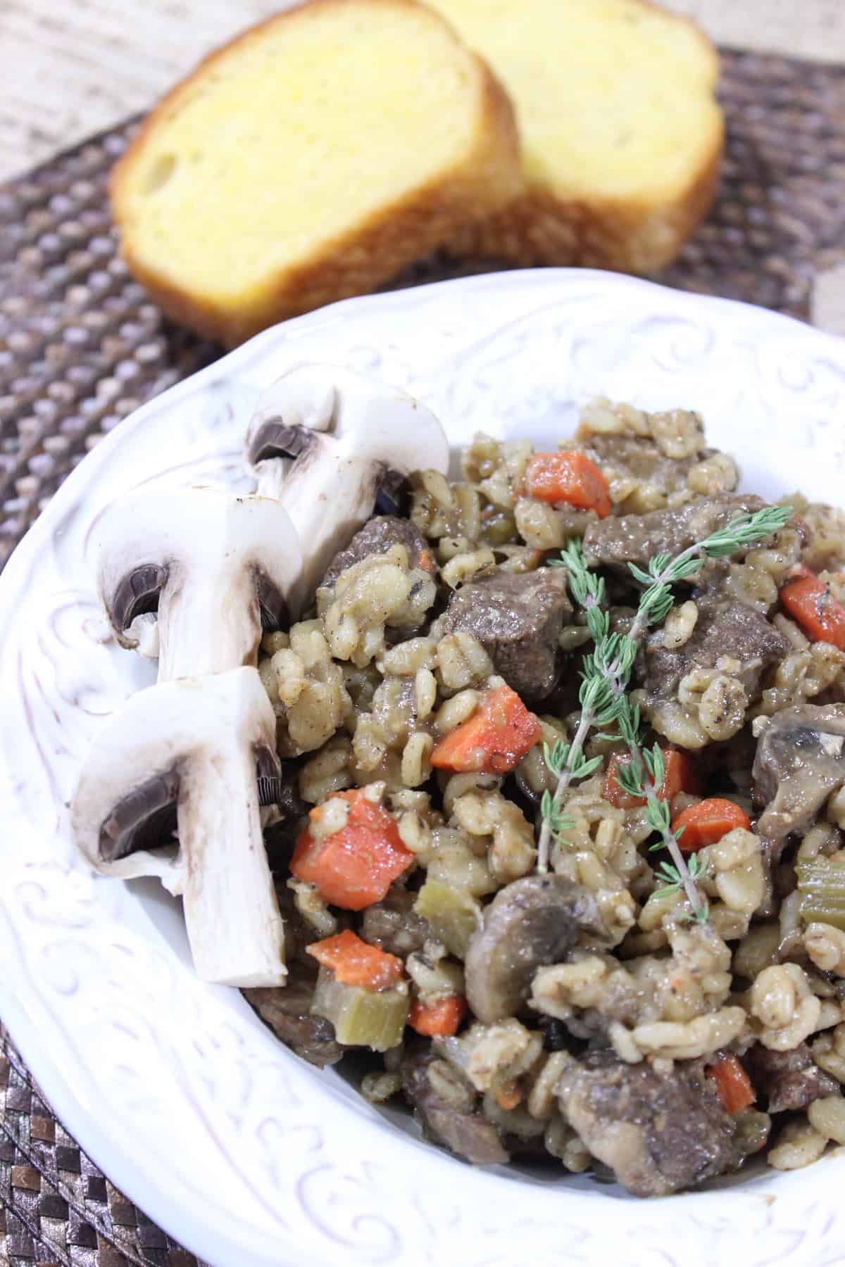Beef Barley Mushroom Stew - www.kudoskitchenbyrenee.com Two slices of toast next to a serving bowl of beef, barley, and mushroom stew with sliced mushrooms on the side.