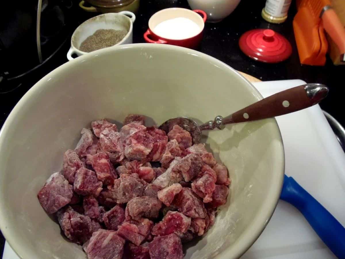 Beef cubes dusted with flour in a large bowl with a spoon.