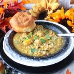 A creamy bowl of chicken and wild rice soup topped with arugula, a biscuit and a spoon inside the bowl.