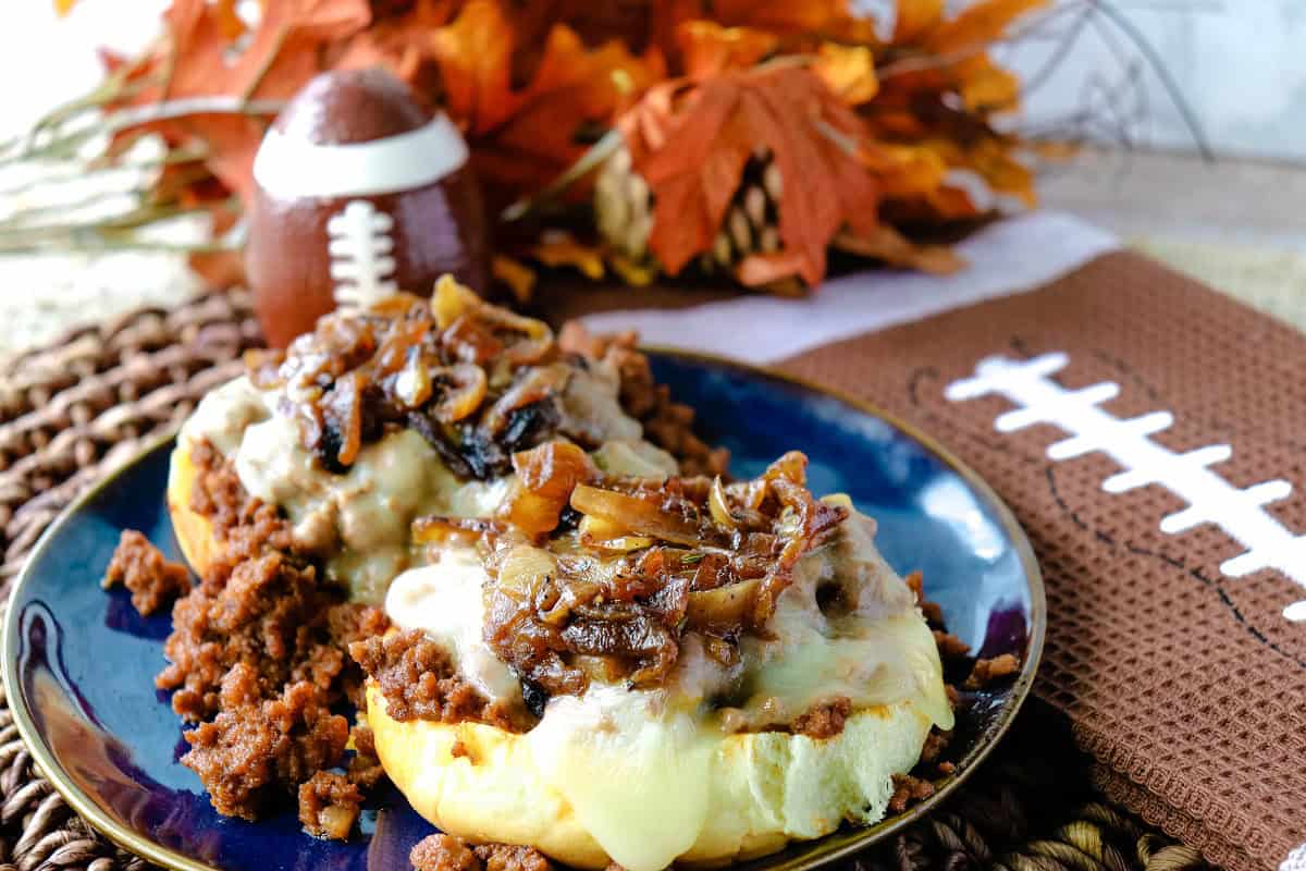 An open face French onion sloppy joe sandwich on a blue plate with a football napkin on the side.