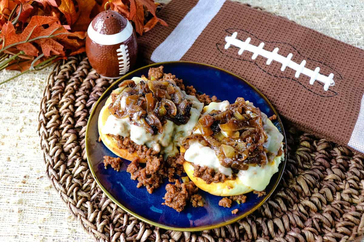 A football salt shaker and napkin behind a plate holding a French onion sloppy joe sandwich.