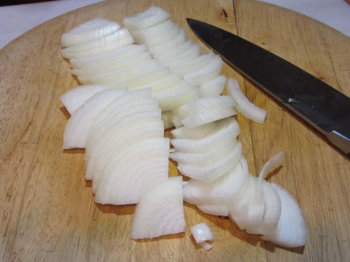 Sliced sweet onions on a wooden cutting board next to a knife.