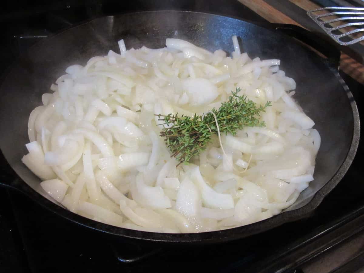 Sliced onions and a thyme bouquet in a cast iron skillet before caramelizing.