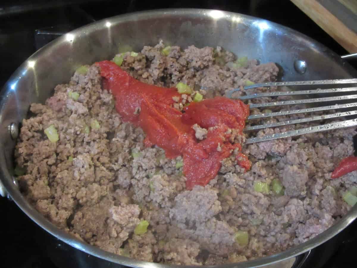 Tomato past in a large skillet with browned ground beef for making sloppy joes.