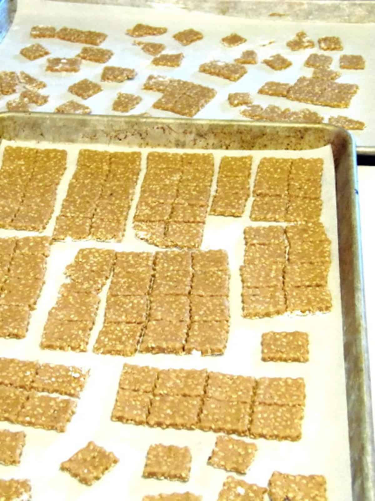Sesame seed crackers before baking on a countertop and on a baking sheet.