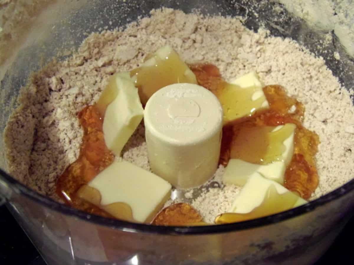 Flour, butter, and honey inside the bowl of a food processor.