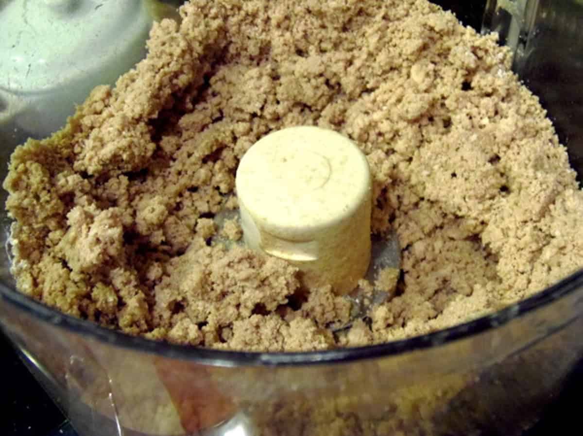 A sandy looking dough inside the bowl of a food processor.