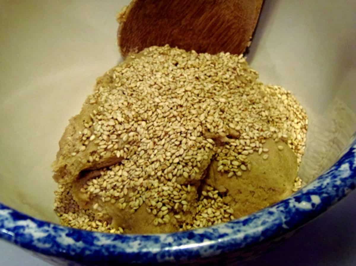 Toasted sesame seeds sitting on top of raw cracker dough in a bowl.