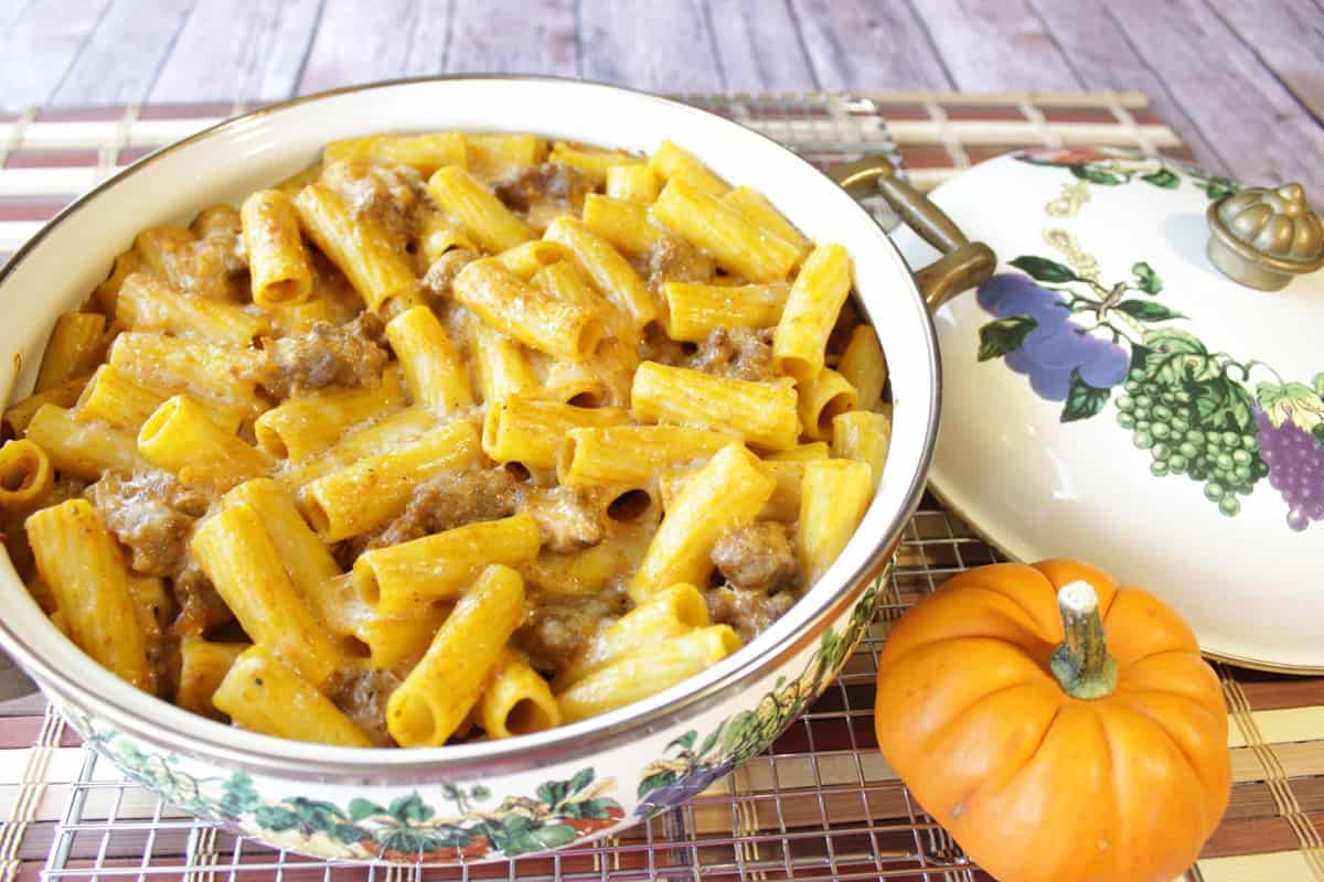 A creamy looking pasta with pumpkin cream sauce in a casserole dish along with a small pumpkin on the side.