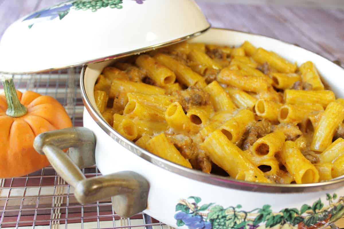 A casserole dish with pumpkin cream pasta with bratwurst along with a cover on the side.