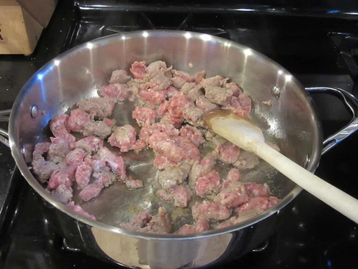 Browning crumbled bratwurst in a large skillet on the stovetop.