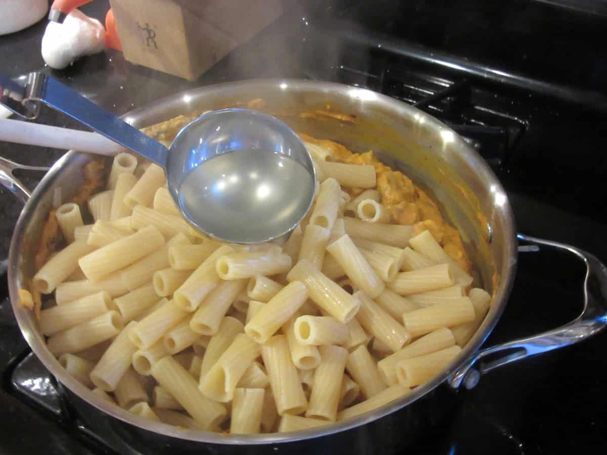 Cooked rigatoni in a skillet with pasta cooking water being poured over it.