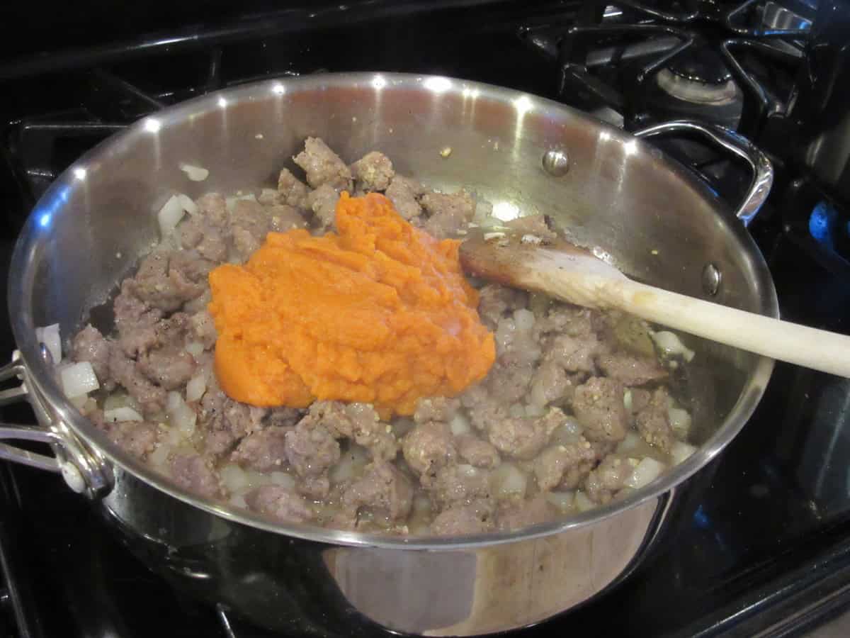 Cooked bratwurst and pumpkin puree in a large skillet on the stovetop.