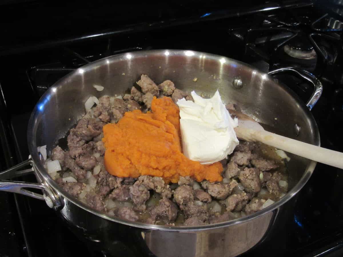 Cooked bratwurst crumbles with onions, pumpkin puree, and cream cheese in a large skillet.