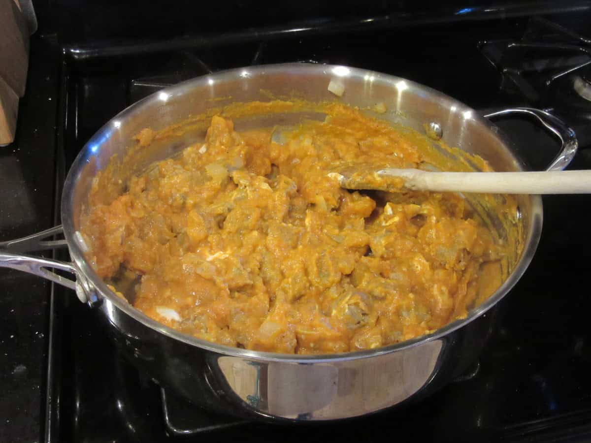 A large high-sided skillet with cooked bratwurst and pumpkin cream sauce.