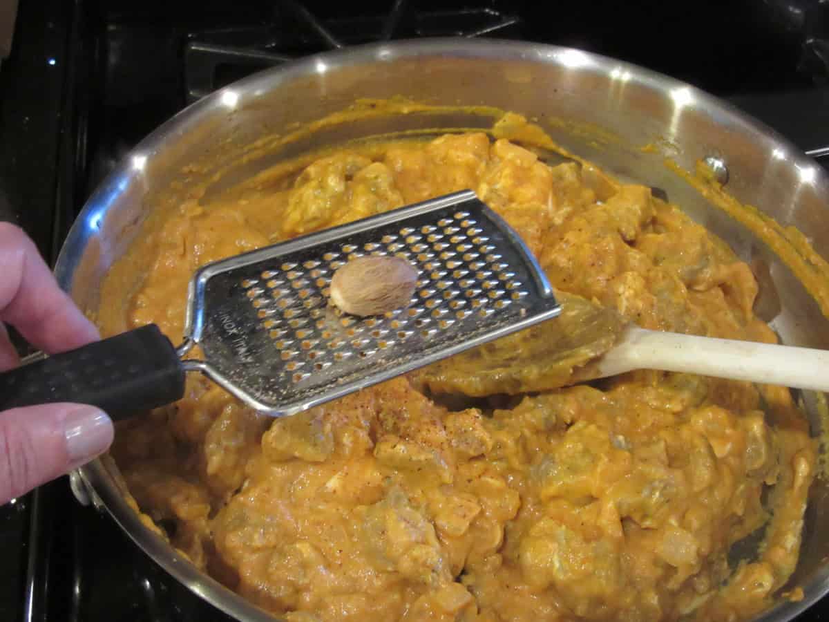 A nutmeg pod on a grater being grated into a pan of bratwurst and pumpkin sauce.