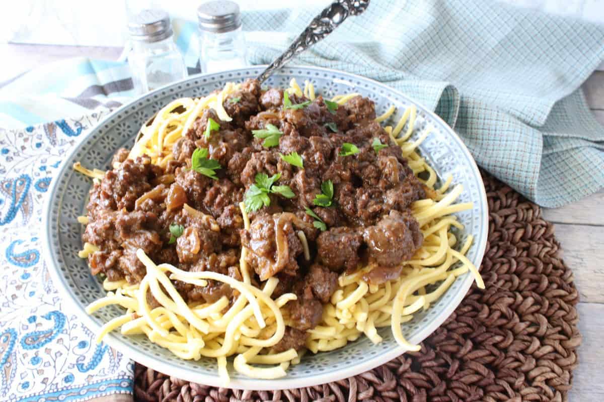 A blue bowl filled with ground beef sauerbraten covered spaetzle on a brown placemat.
