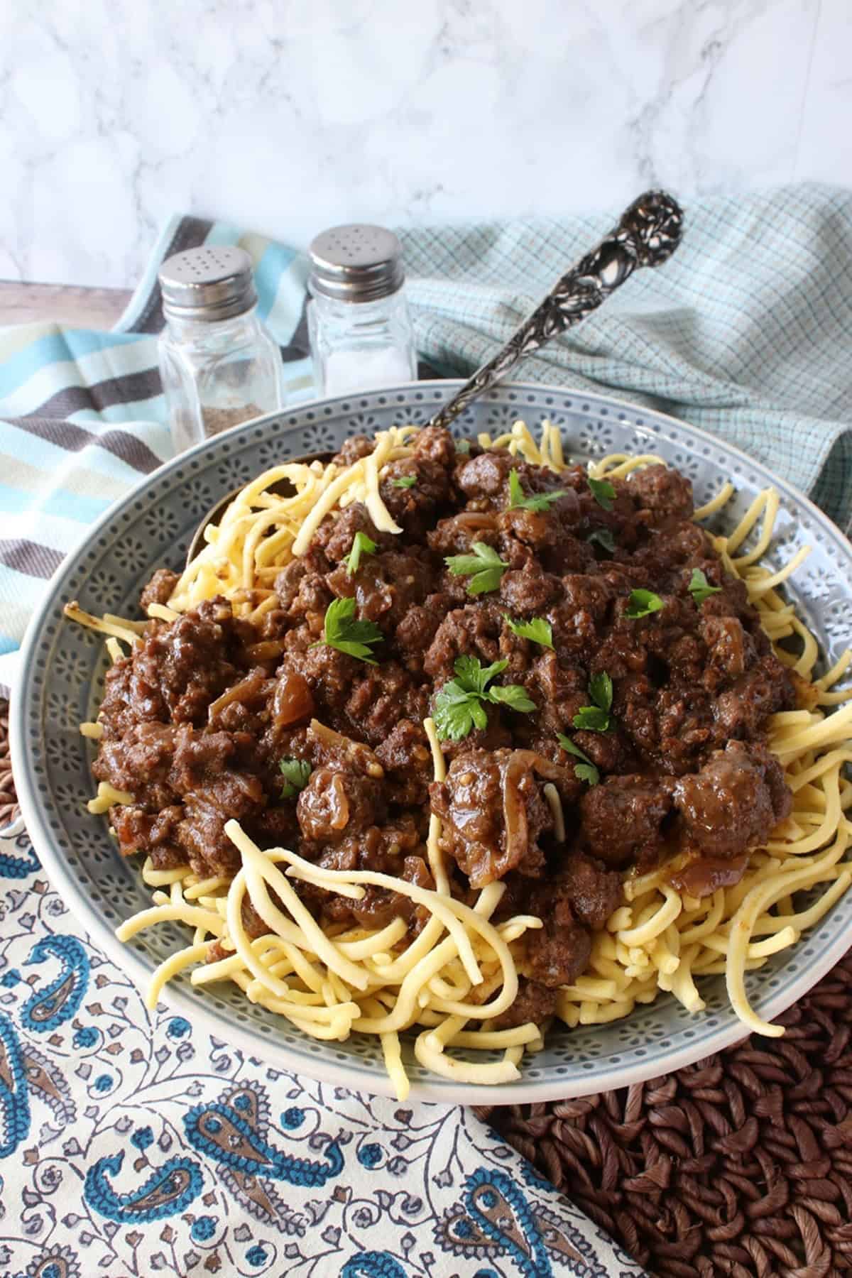 German spaetzle noodles covered with ground beef goulash sauce in a blue bowl.