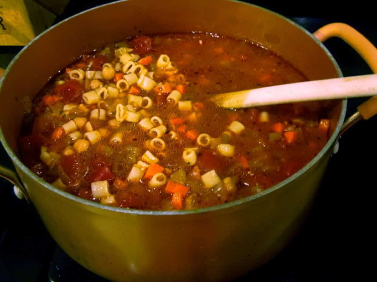 A soup pot filled with Tuscan pasta soup on the stovetop along with a wooden spoon.