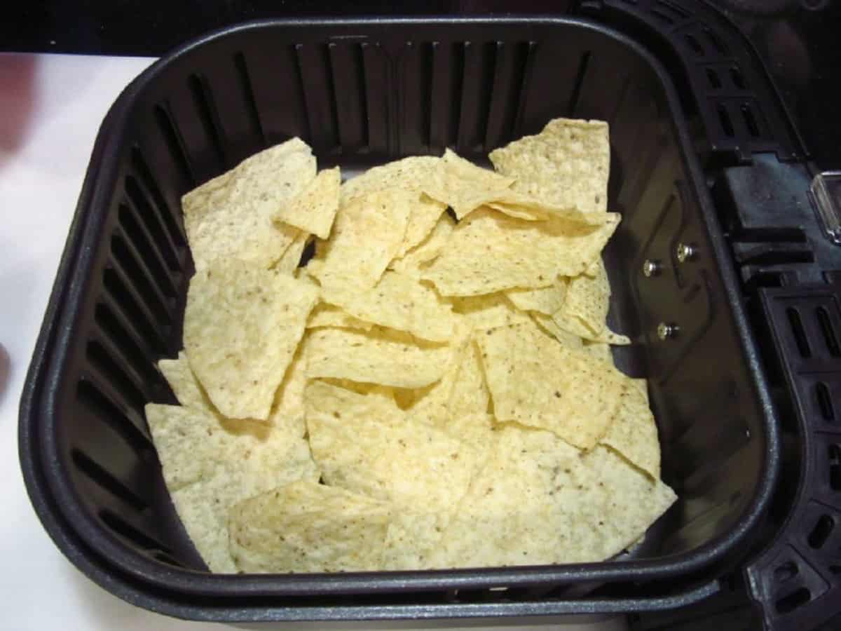 A layer of corn nacho chips in the bottom of an air fryer basket.