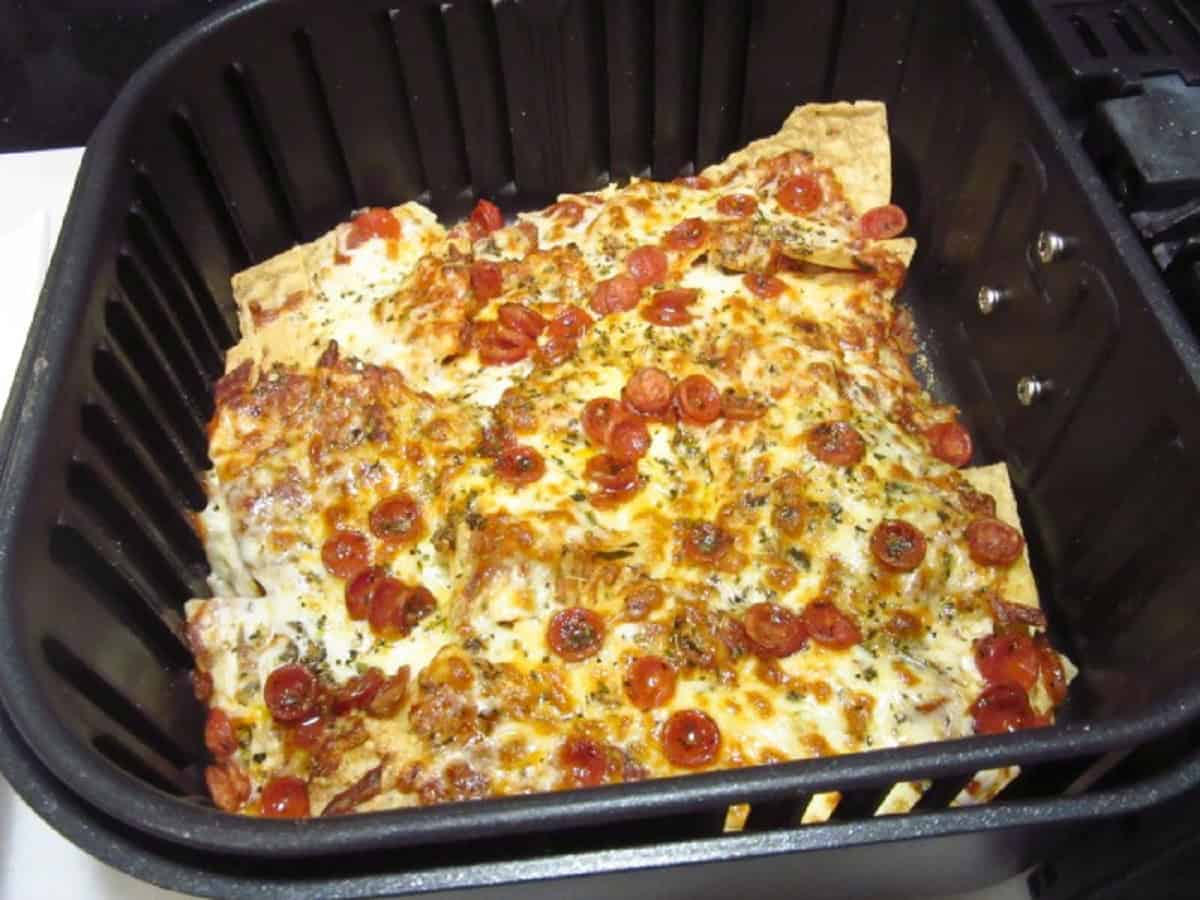 Browned and cheesy pizza nachos in an air fryer basket.