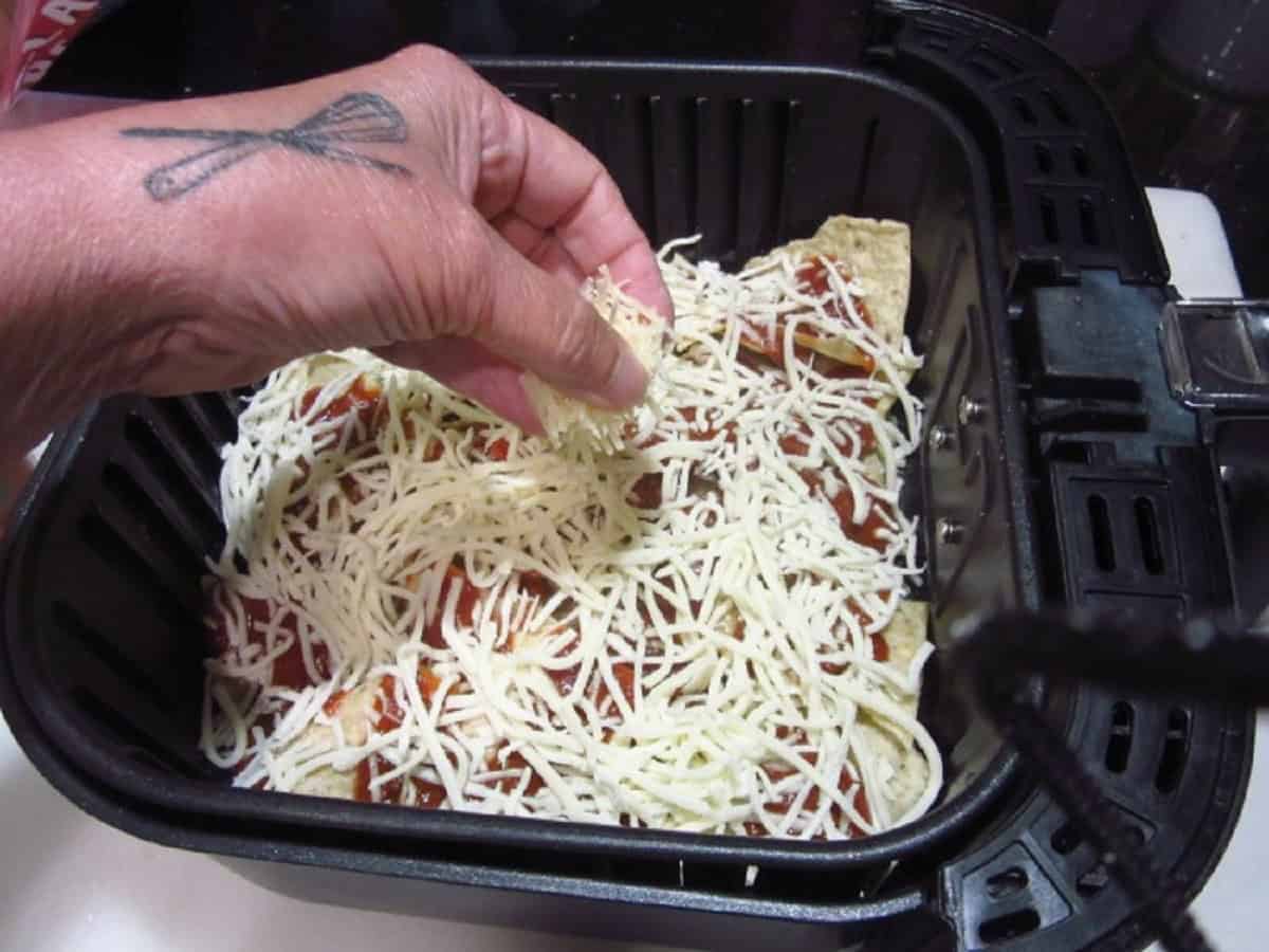 Shredded mozzarella cheese being added to an air fryer basket for making nachos.
