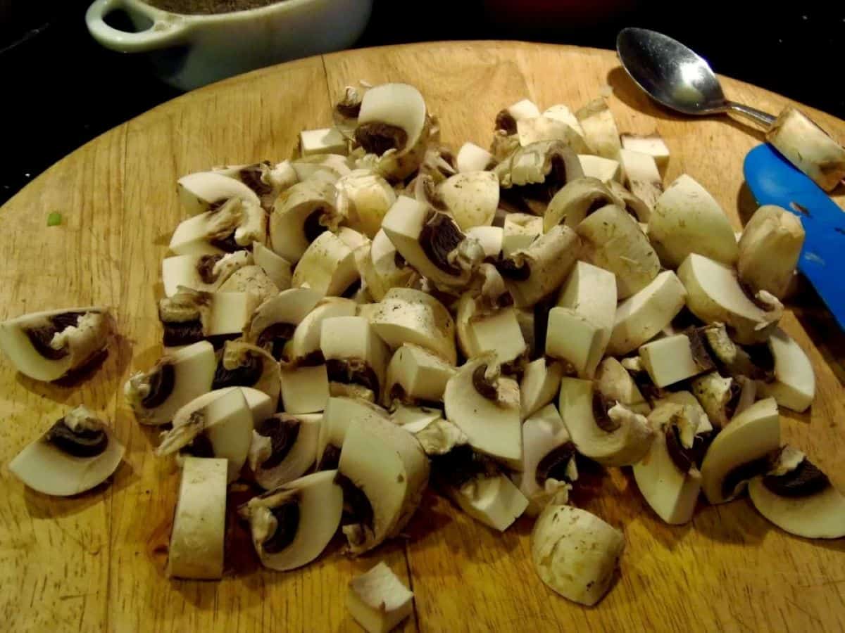 Quartered mushrooms on a wooden cutting board.