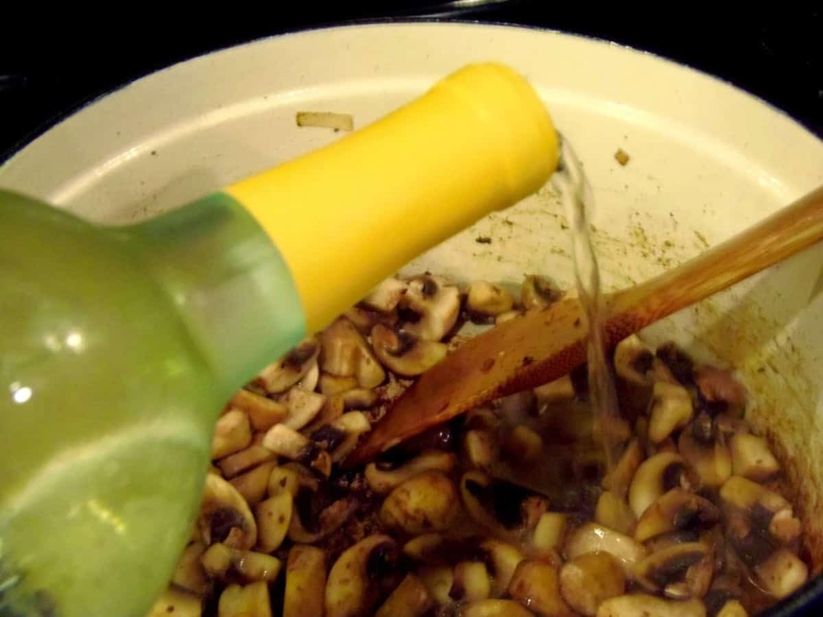 White wine being added to a Dutch oven with sauteed mushrooms.