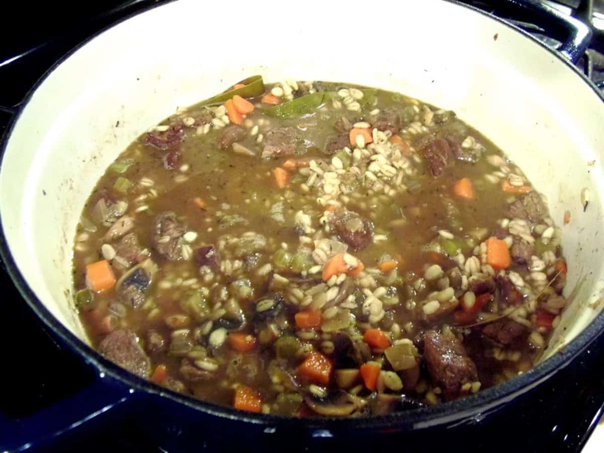 Beef broth, barley, beef, and carrots in a Dutch oven before simmering.