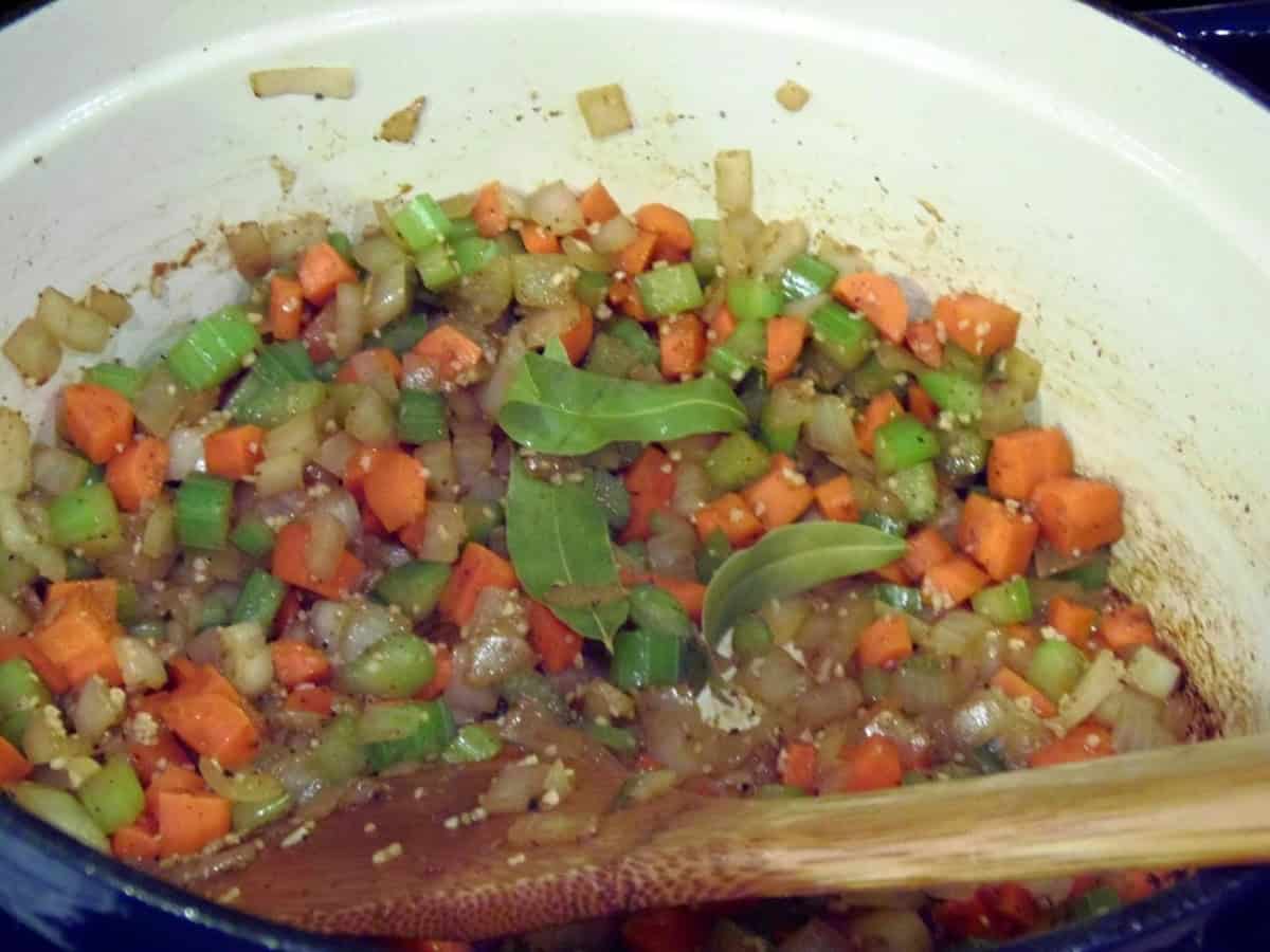 Bay leaves along with stew veggies in a Dutch oven with a wooden spatula.