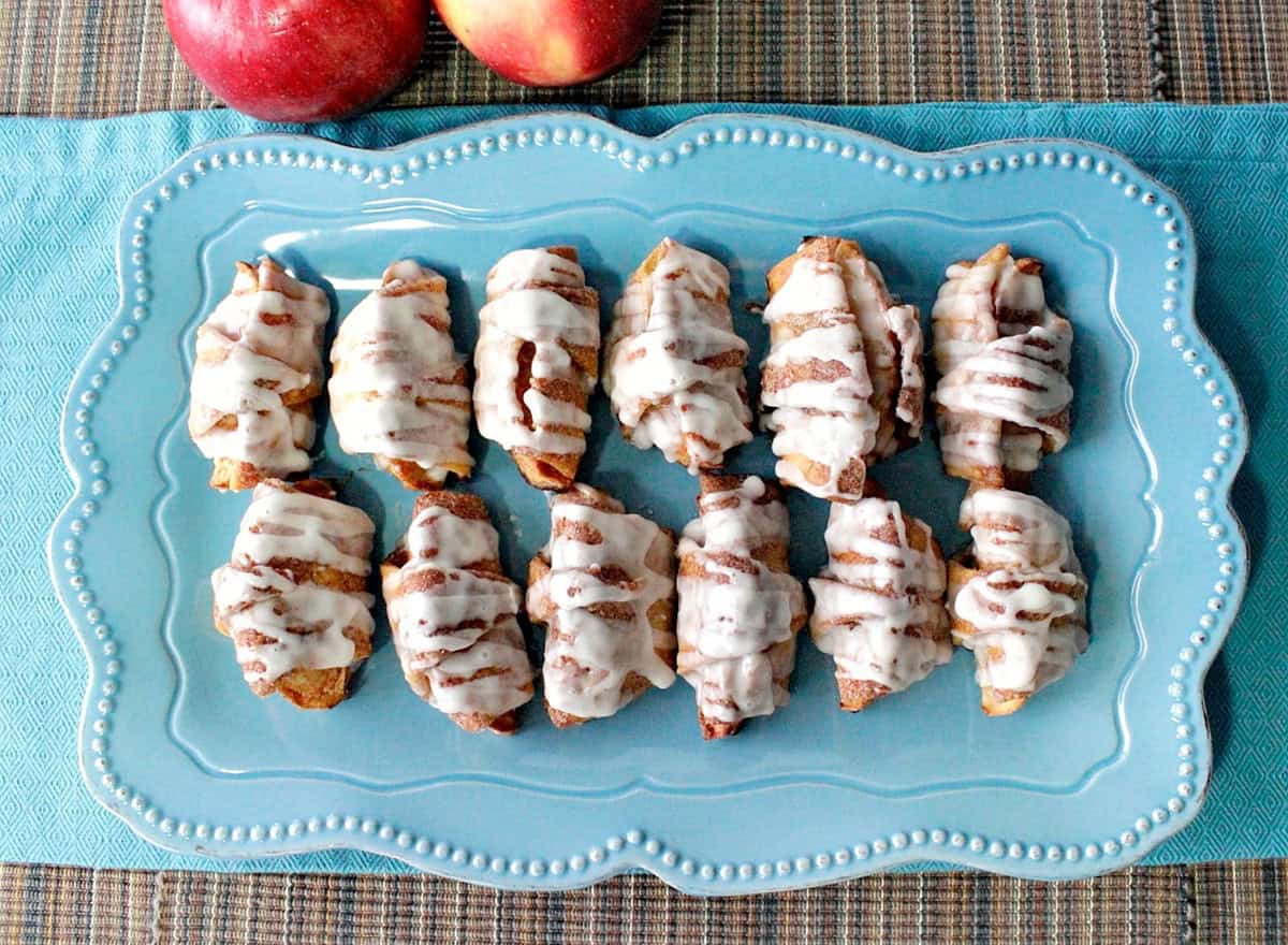 Twelve glazed apple pie wedges on a blue platter.