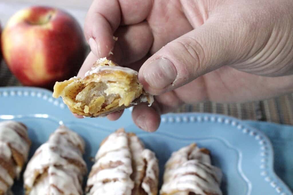 A hand holding an apple pie wedge with a bite taken.