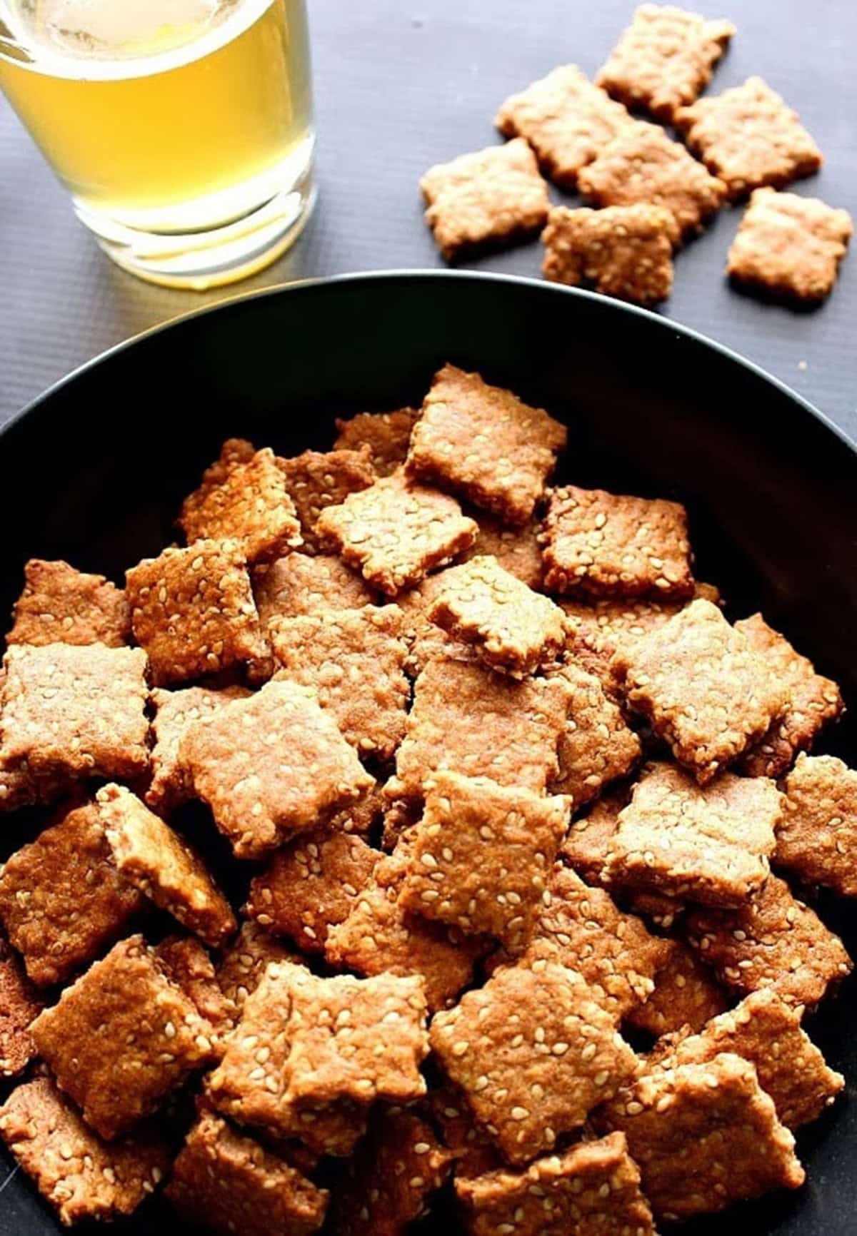 A glass of beer in the background of a bowl of homemade sesame seed crackers.