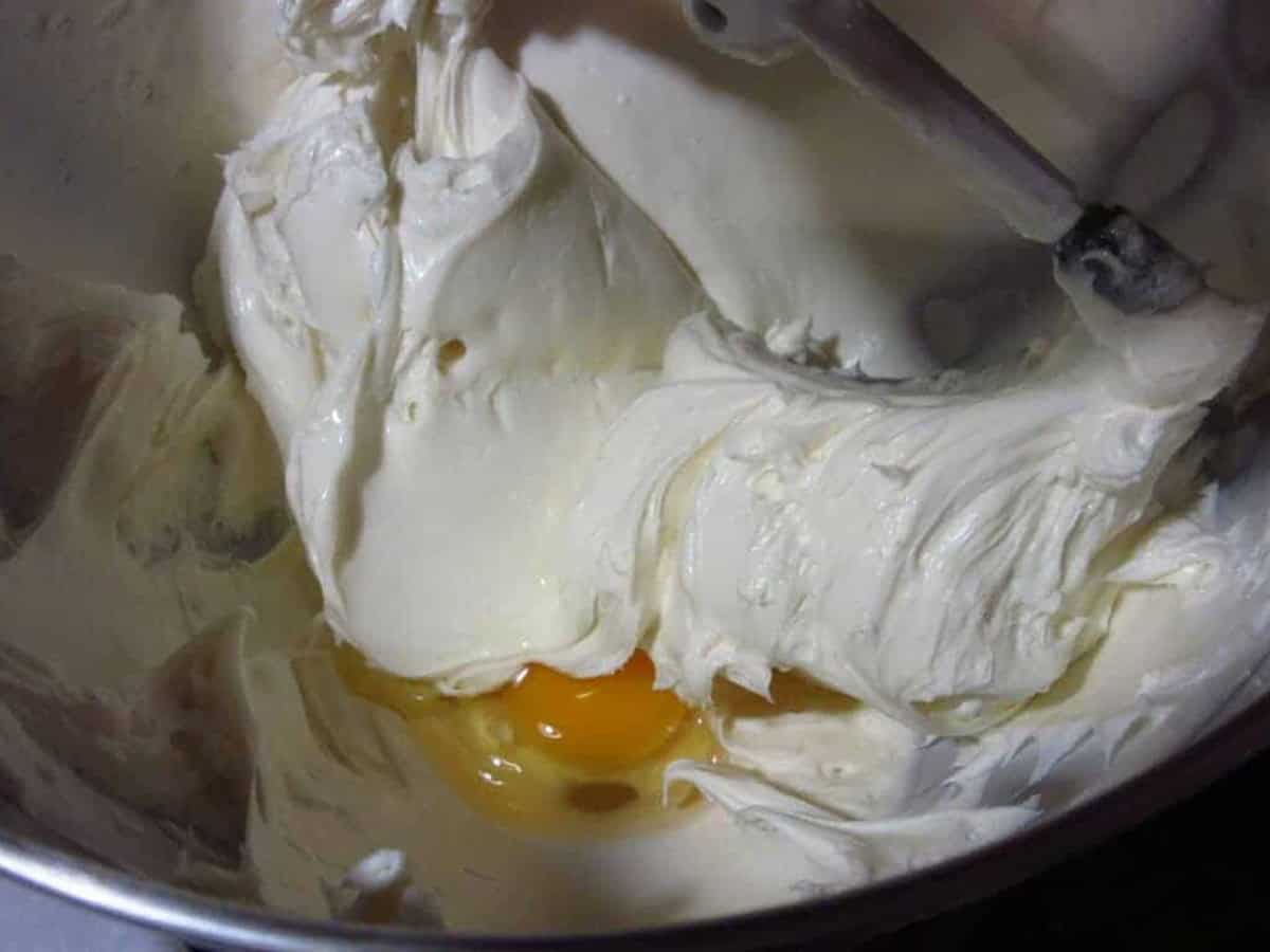 Creamy cheesecake filling with an egg being beaten into it with a stand mixer.