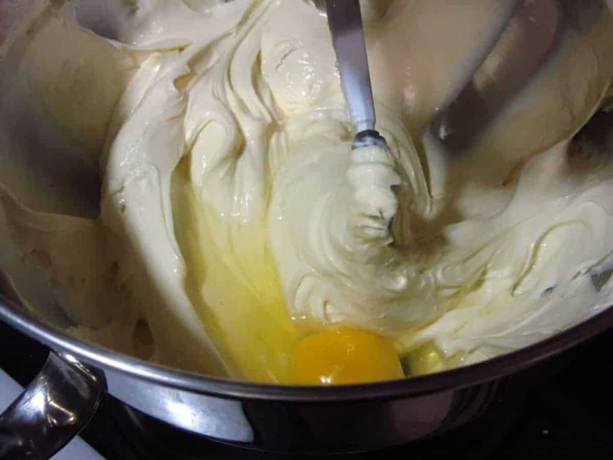 Creamy cheesecake filling being beaten in a stand mixer with an egg.