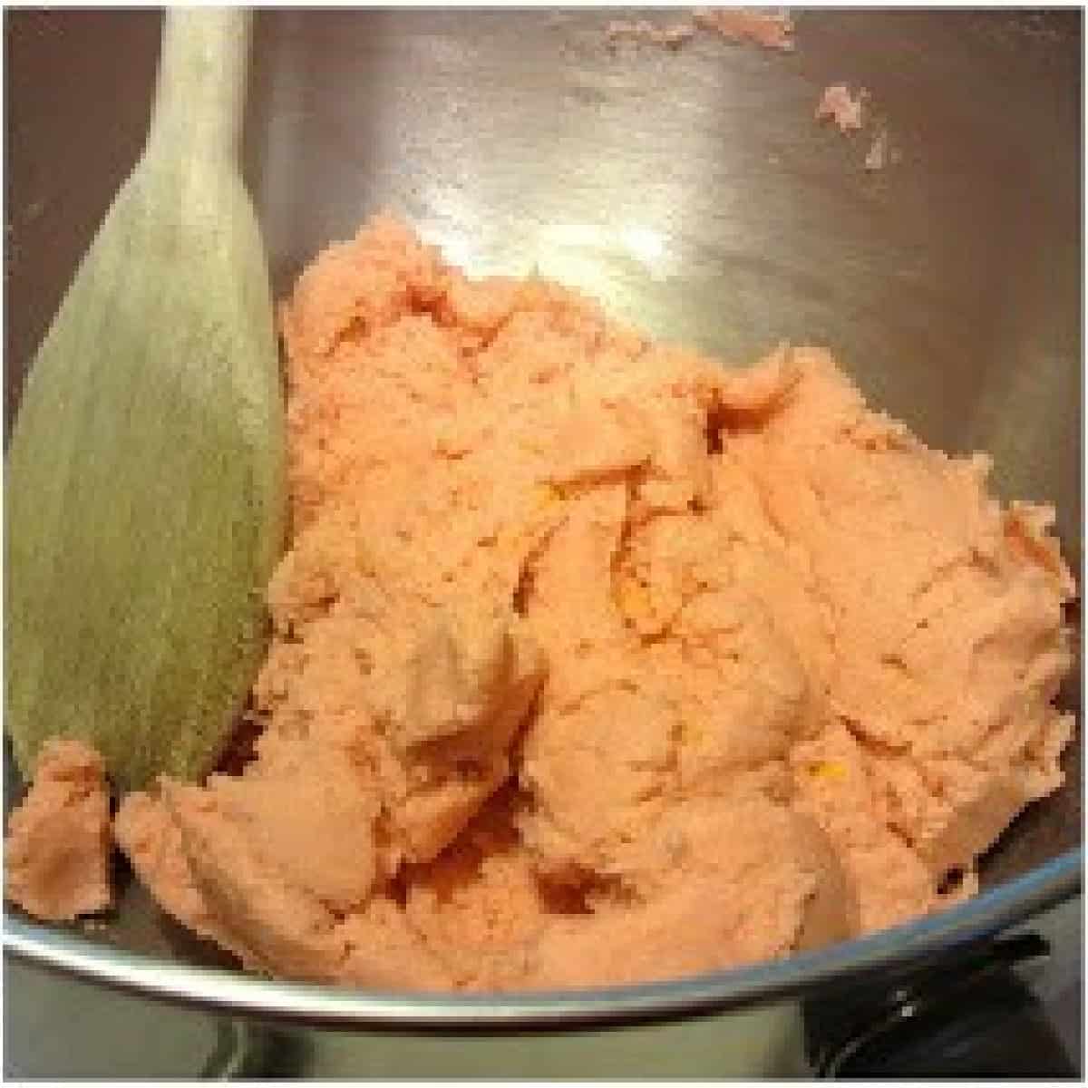 A pink cookie dough with a wooden spoon in a silver bowl.