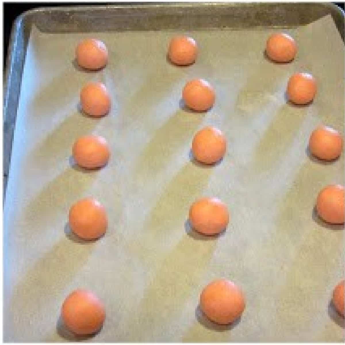 Pink balls of cookie dough on a sheet of parchment on a baking sheet.