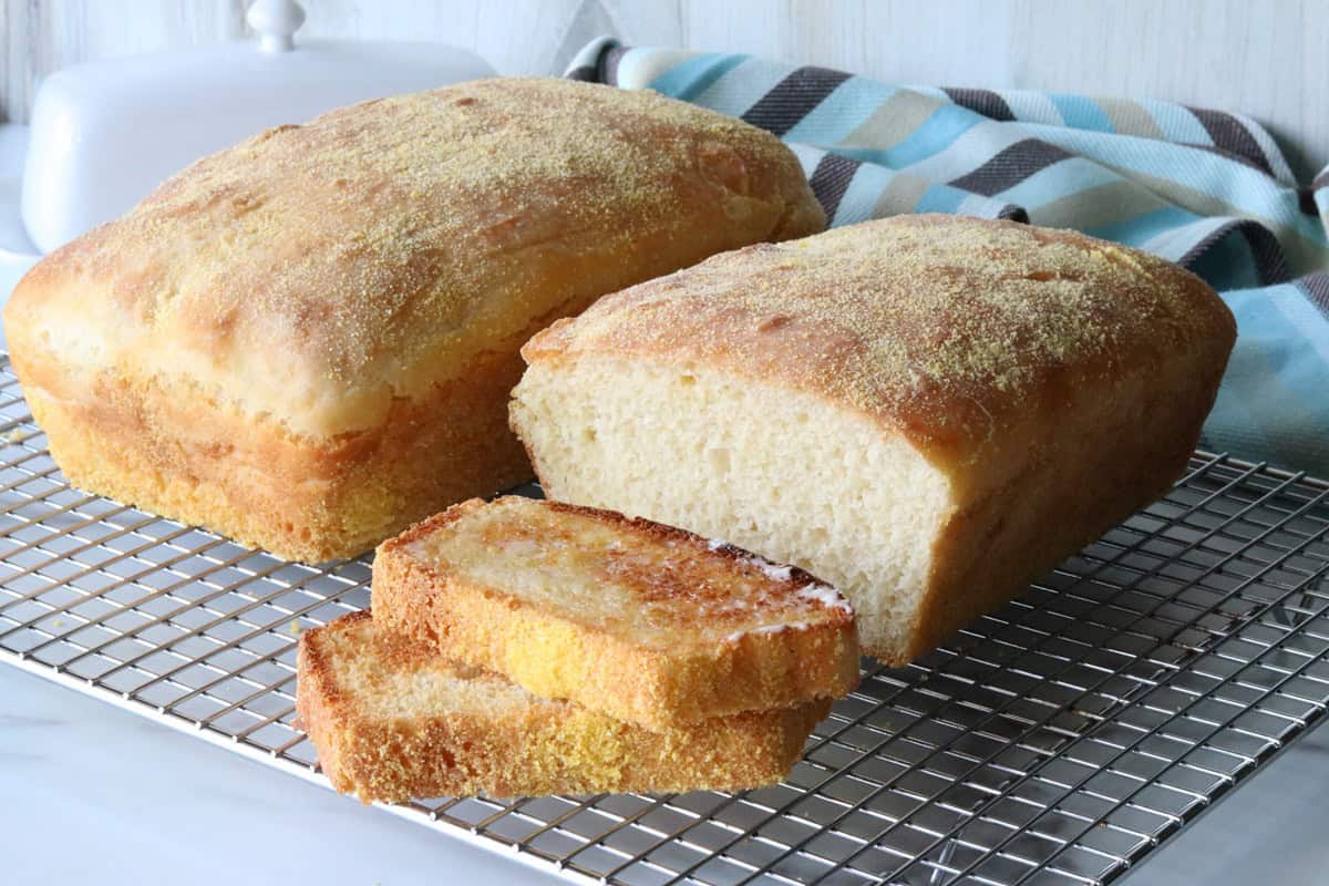 A wire rack with two baked English muffin bread loaves along with a blue and brown napkin in the background.