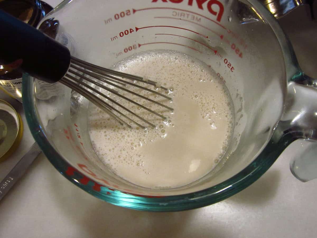 A small whisk in a glass measuring cup with dissolved yeast and water.