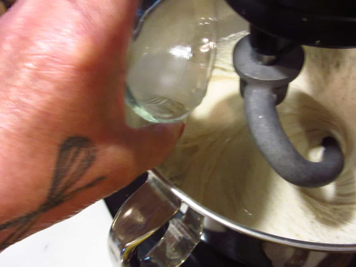 Baking soda and water being added to the English muffin bread dough in a stand mixer.