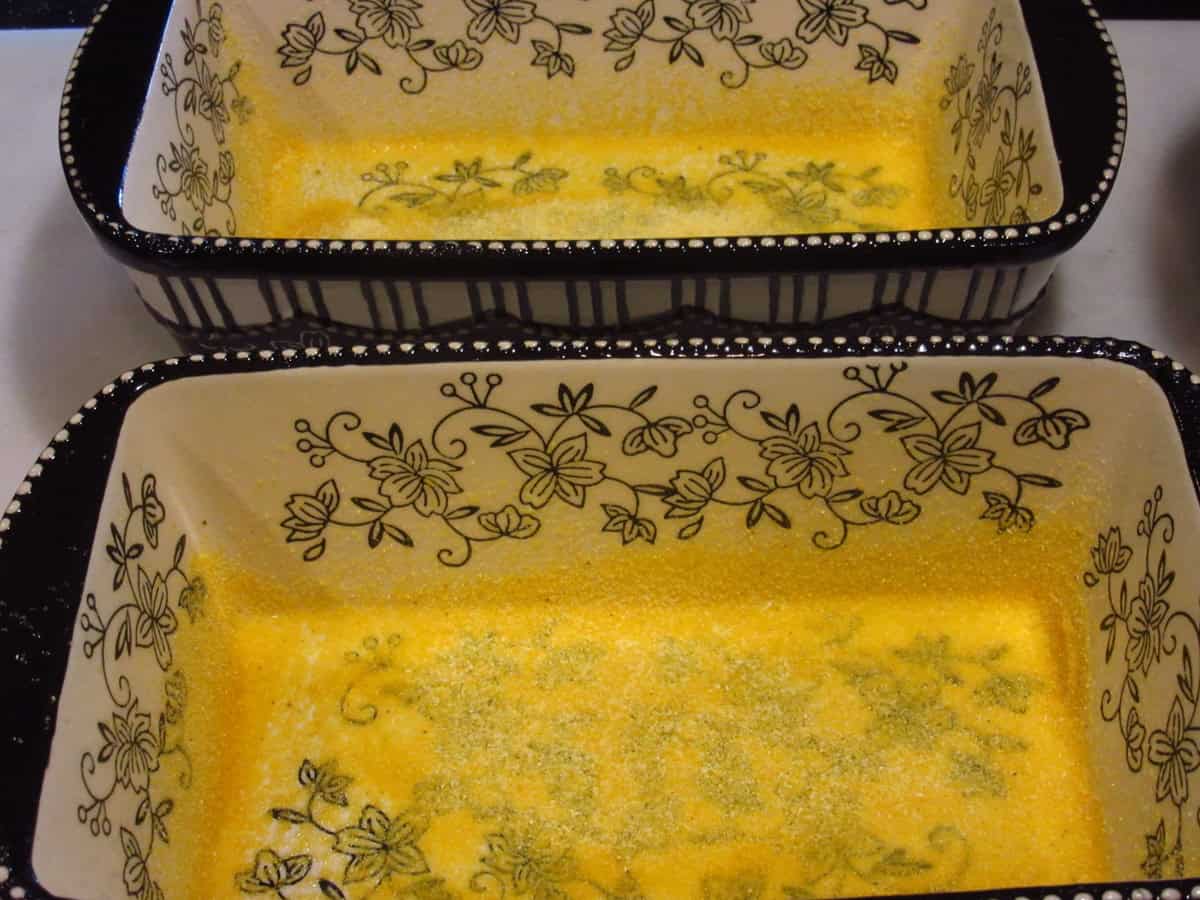 Two ceramic loaf pans with cornmeal on the bottom and up the sides of the pan.