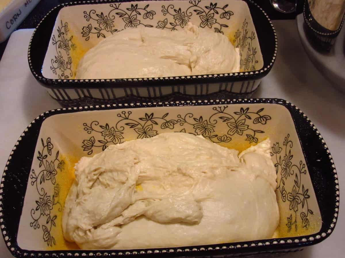 Two loaf pans with a soft sticky dough in each for making English muffin bread.