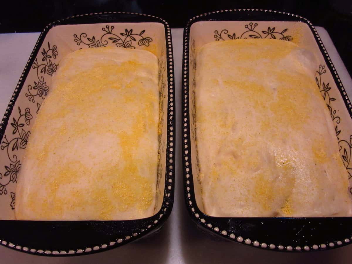 Two cornmeal dusted, unbaked English muffin bread in ceramic loaf pans.